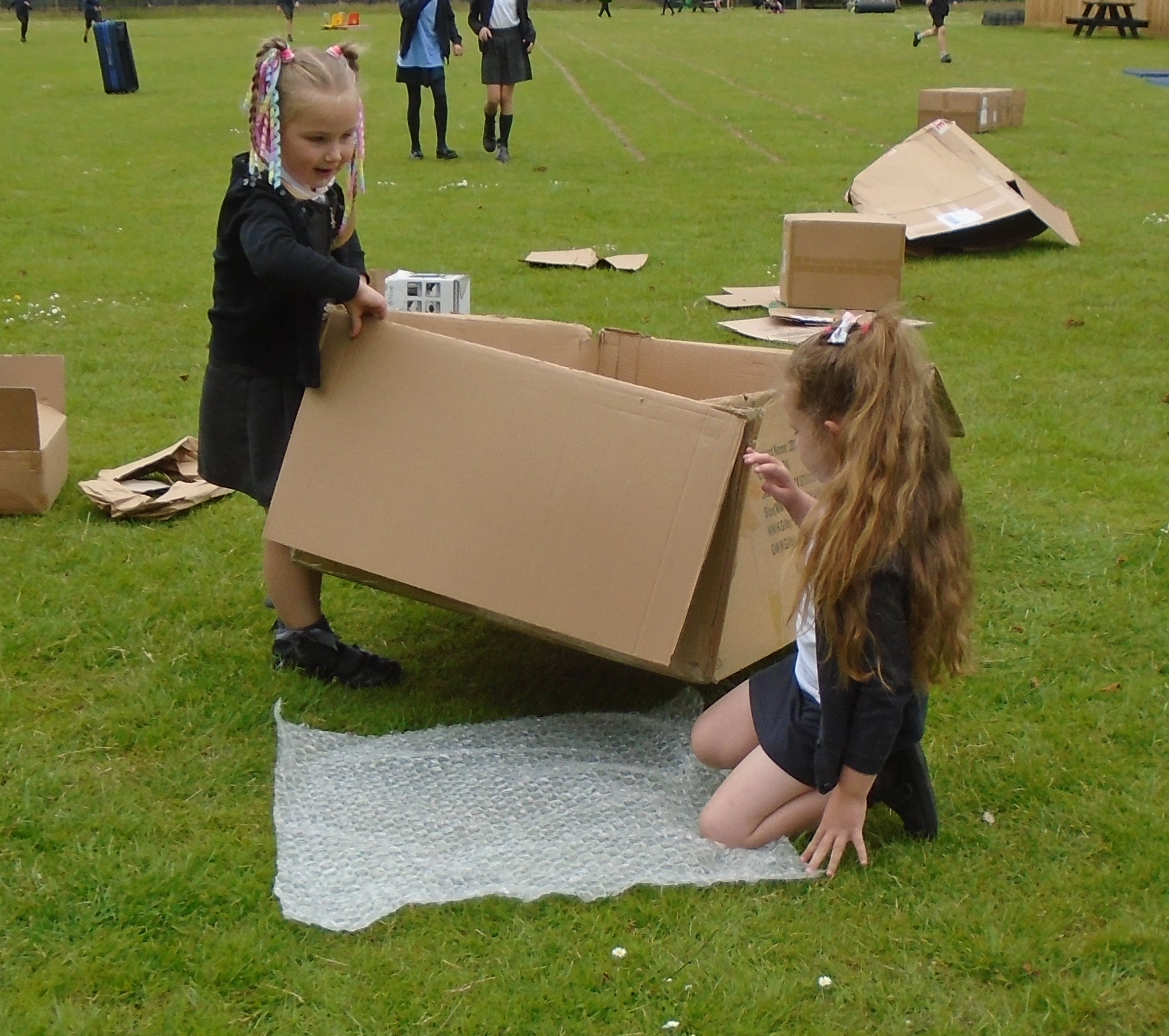 Two children playing with boxes in the school field.