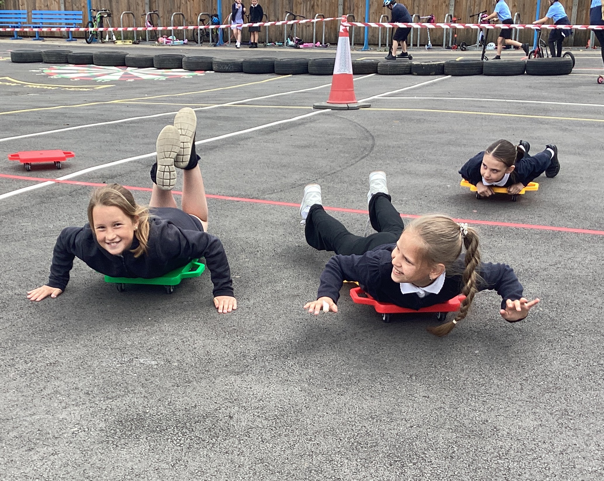 Two children lying on wheeled boards, rolling along on the playground.
