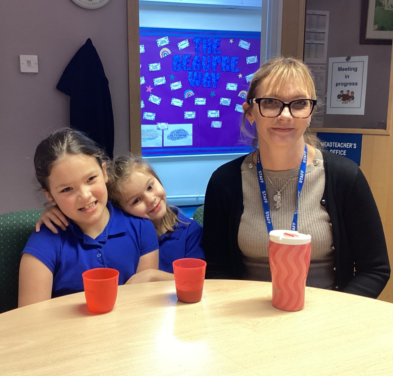 Two children sitting and smiling with the headteacher. 